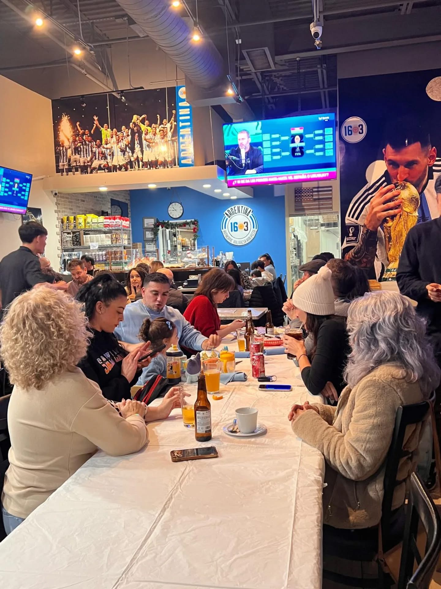 Mesa larga llena de familia y amigos disfrutando junto al mural de Messi